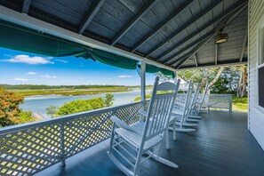 A covered porch with white rocking chairs, a view of a river, and a green canopy.