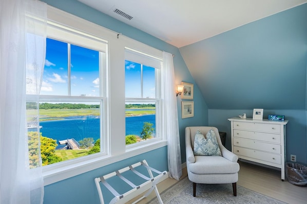 A room with a view of a lake, a chair, a dresser, and a ladder.