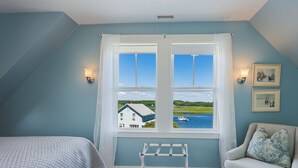 Une chambre avec vue sur un lac et une maison, comprenant un lit, une chaise et un étendoir.