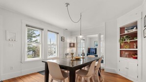 A dining area with a wooden table, white chairs, a pendant light, and a view of the outdoors. - Helena House: Charming and serene, close to Plum Cove Beach (Gloucester)