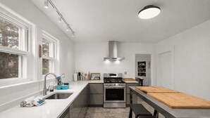 A modern kitchen with a stainless steel stove, a built-in oven, a large window, and a wooden cutting board on the counter. - Helena House: Charming and serene, close to Plum Cove Beach (Gloucester)