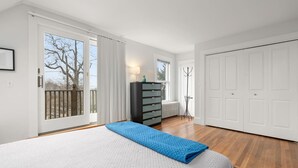 A bedroom with a large bed, a dresser, a radiator, and a door leading to a balcony. - Helena House: Charming and serene, close to Plum Cove Beach (Gloucester)