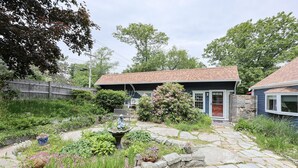 Ein Haus mit einem steinernen Weg, der zu einer Haustür führt, umgeben von üppiger Bepflanzung und einem kleinen Garten mit Vogeltränke.