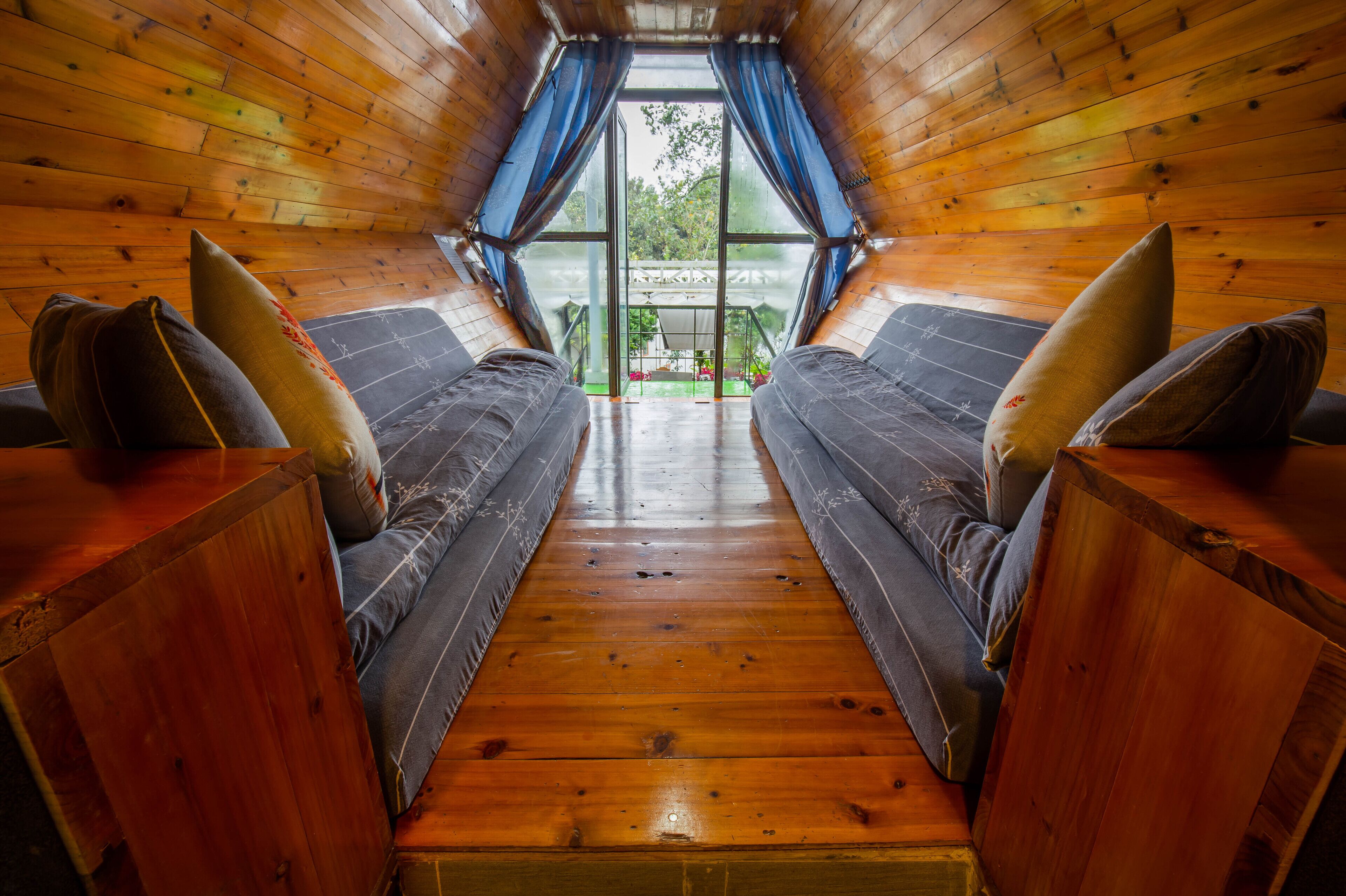 A cozy cabin interior with a wooden floor, two sofas with cushions, and a large window with curtains.