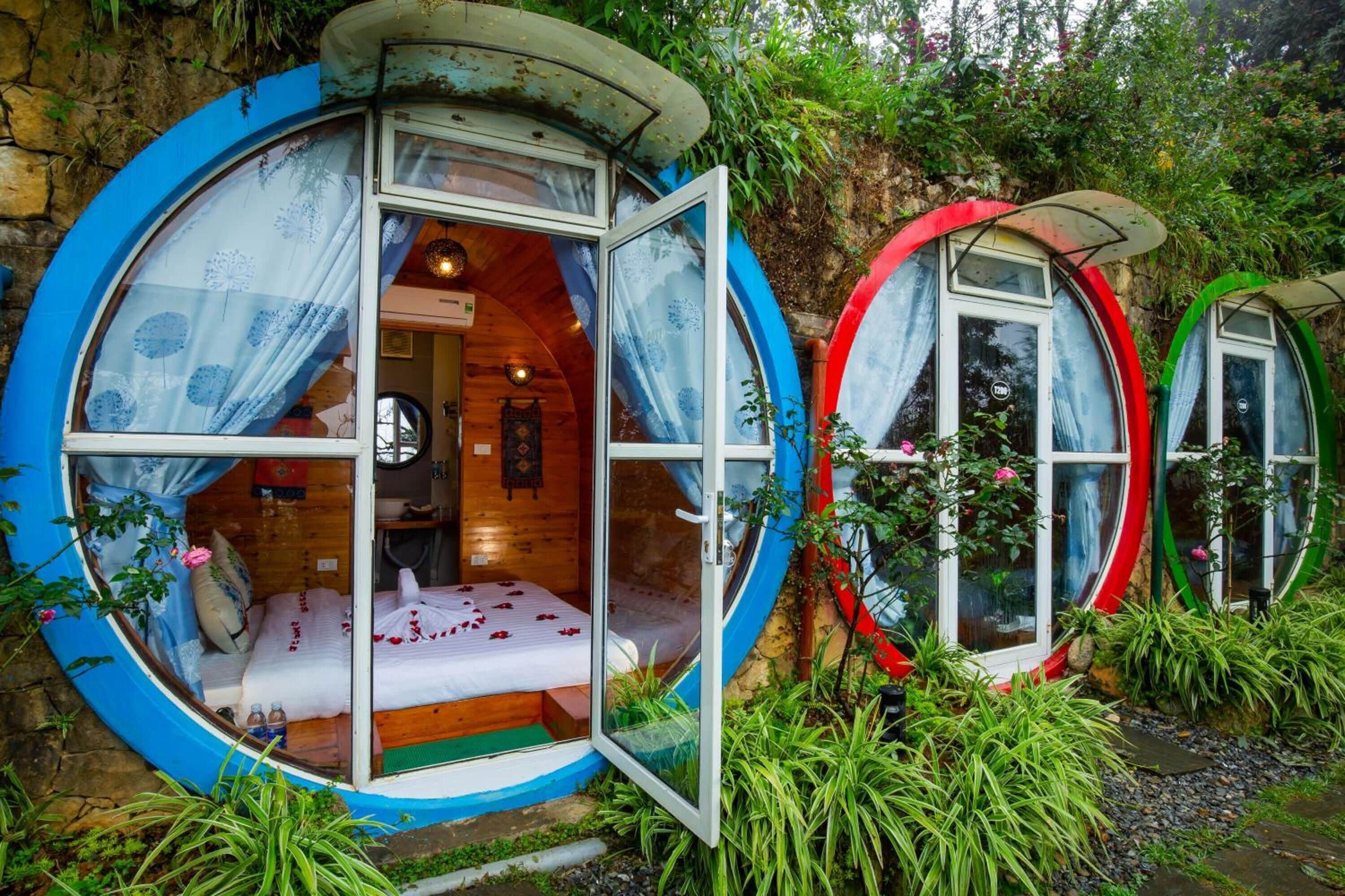 A circular room with a bed and a wooden interior, surrounded by greenery.