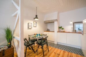 A compact kitchen with a dining area, featuring a wooden floor, a glass table, and a hanging pendant light.