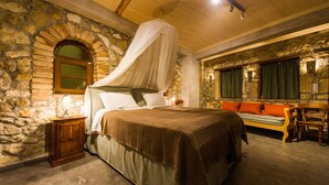Un dormitorio con pared de piedra, una cama con dosel, un banco de madera y una mesita de noche.
