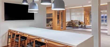 A modern kitchen with a long island counter, bar stools, pendant lighting, and a large flat-screen TV.
