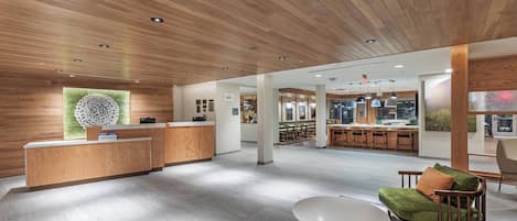 Un lobby espacioso con un mostrador de recepción de madera, un área de descanso con una mesa redonda y una cocina al fondo.