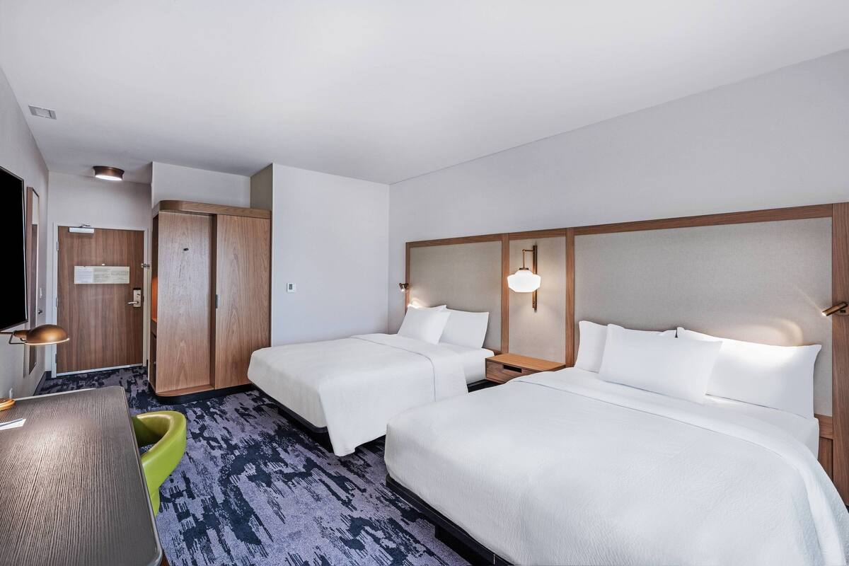 A hotel room with two beds, a desk, a chair, a wardrobe, and a television.