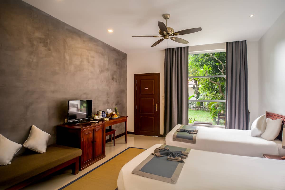 A hotel room with a bed, a sofa, a desk with a TV, and a window with curtains.