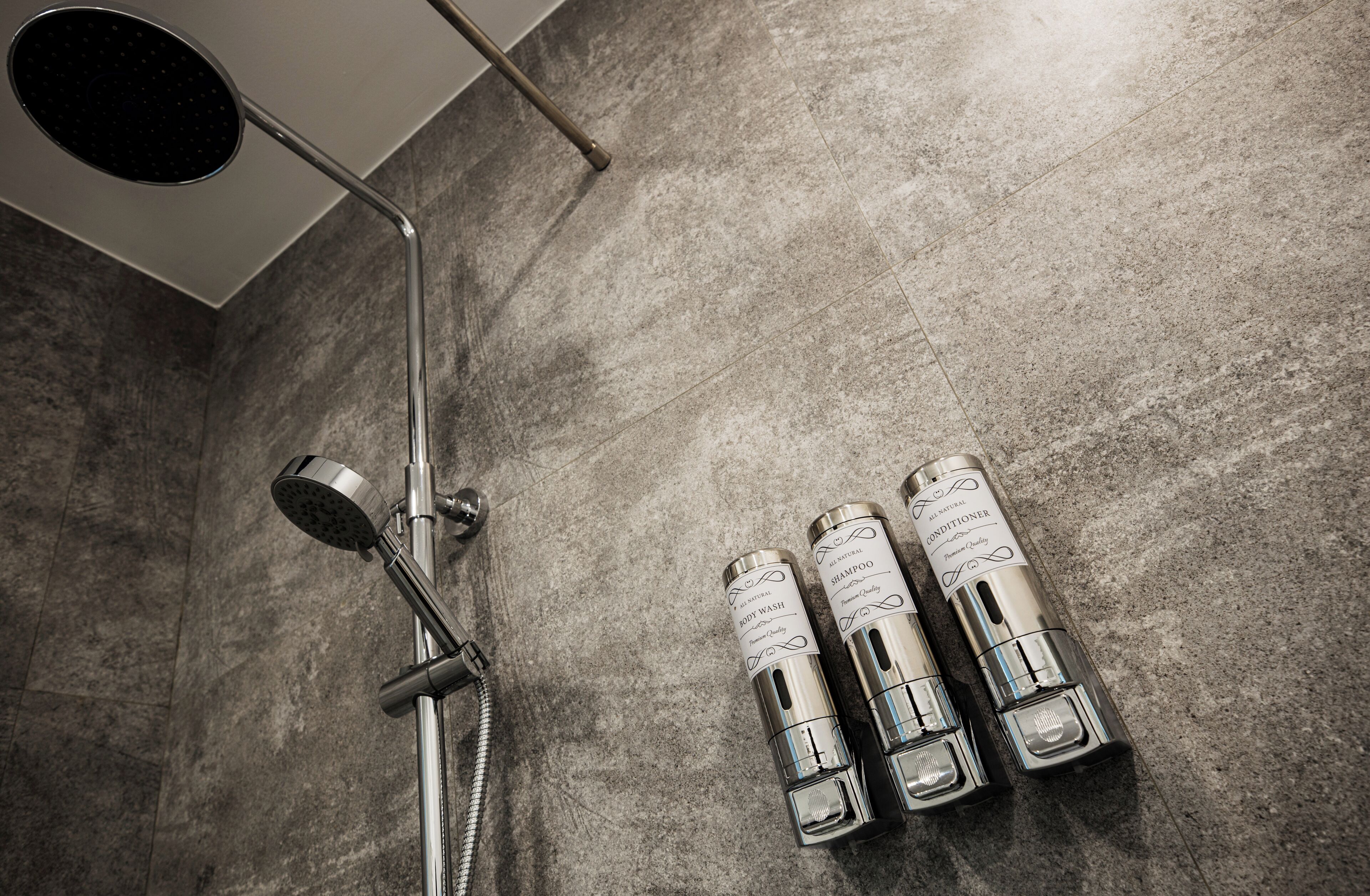 A shower area with a handheld showerhead and two bottles of shampoo and conditioner on the wall.