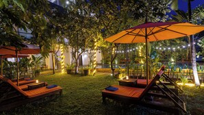 A nighttime outdoor lounge area with wooden loungers, orange umbrellas, and string lights. -  Angkor Serenity Hotel Siem Reap (Siem Reap)