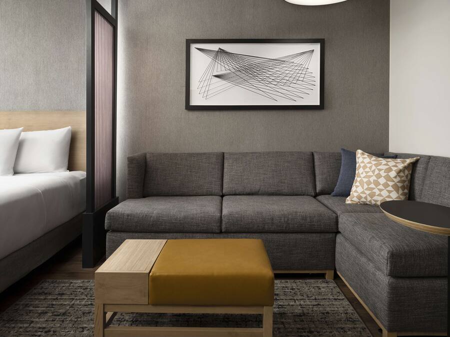 Una sala de estar moderna con un sofá gris, una mesa de centro de madera y una obra de arte abstracta enmarcada en la pared.