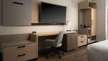 Habitación de hotel con escritorio de madera, una silla, una cama, televisor montado en la pared y un armario con espejo.