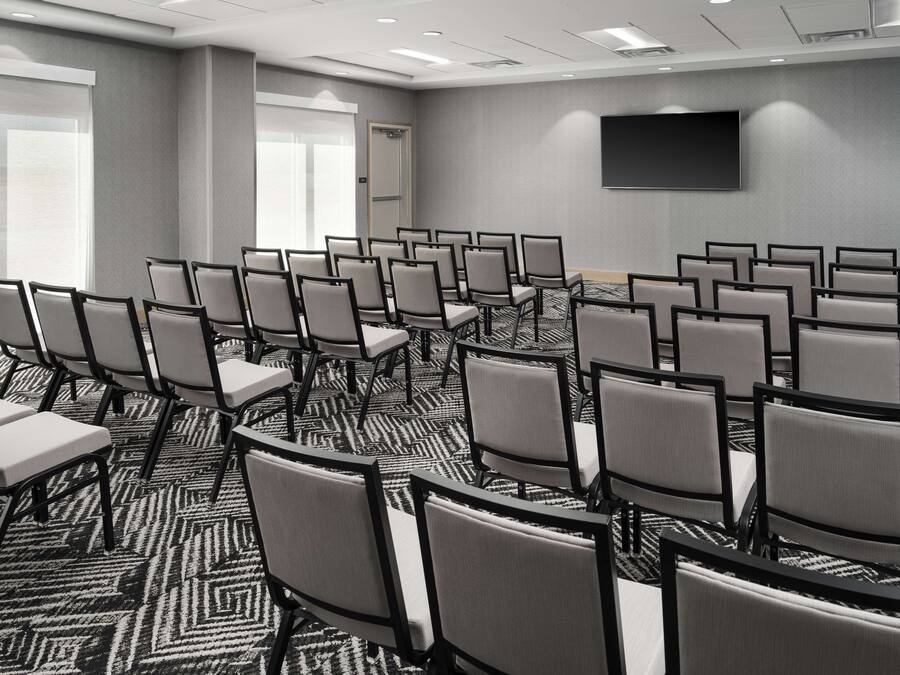 A conference room with rows of chairs, a carpeted floor, and a flat-screen TV on the wall.