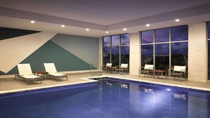 An indoor swimming pool with lounge chairs and a view of the night sky through large windows. - Hyatt Place Amarillo-West (Amarillo)