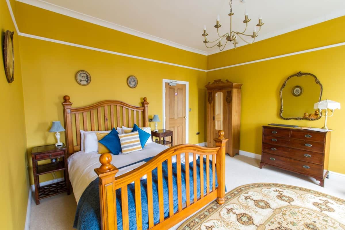 A bedroom with a wooden bed, a nightstand, a dresser, a mirror, and a chandelier.