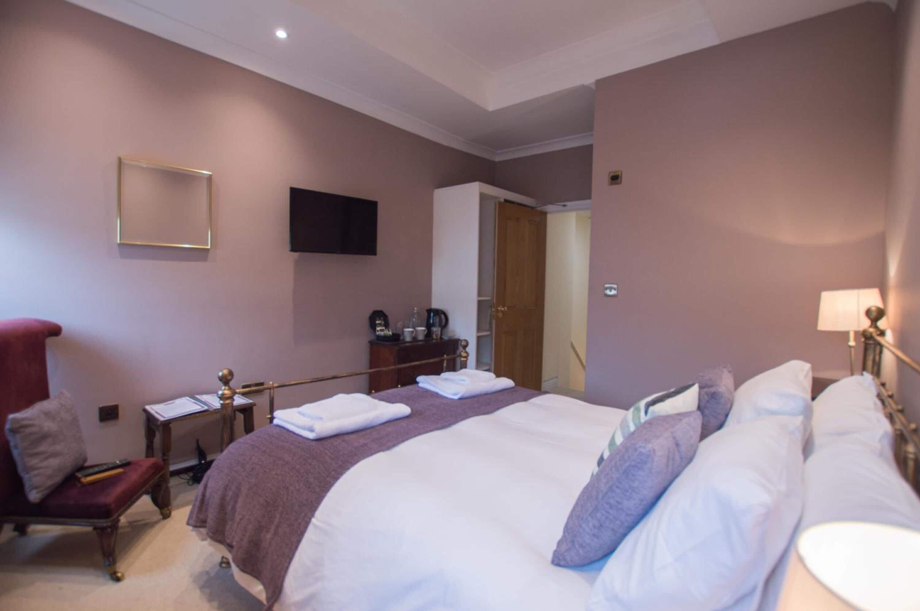 A hotel room with a large bed, a desk with a chair, a TV mounted on the wall, and a wardrobe.