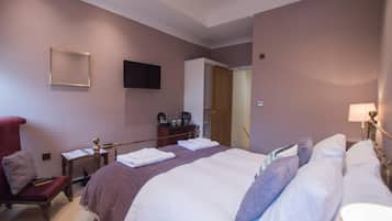A hotel room with a large bed, a desk with a chair, a TV mounted on the wall, and a wardrobe.