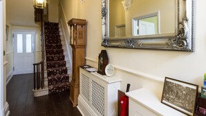 A staircase with a patterned carpet, a wooden grandfather clock, a white console table with a framed picture, and a large ornate mirror. - The Portland Guesthouse (Cheltenham)