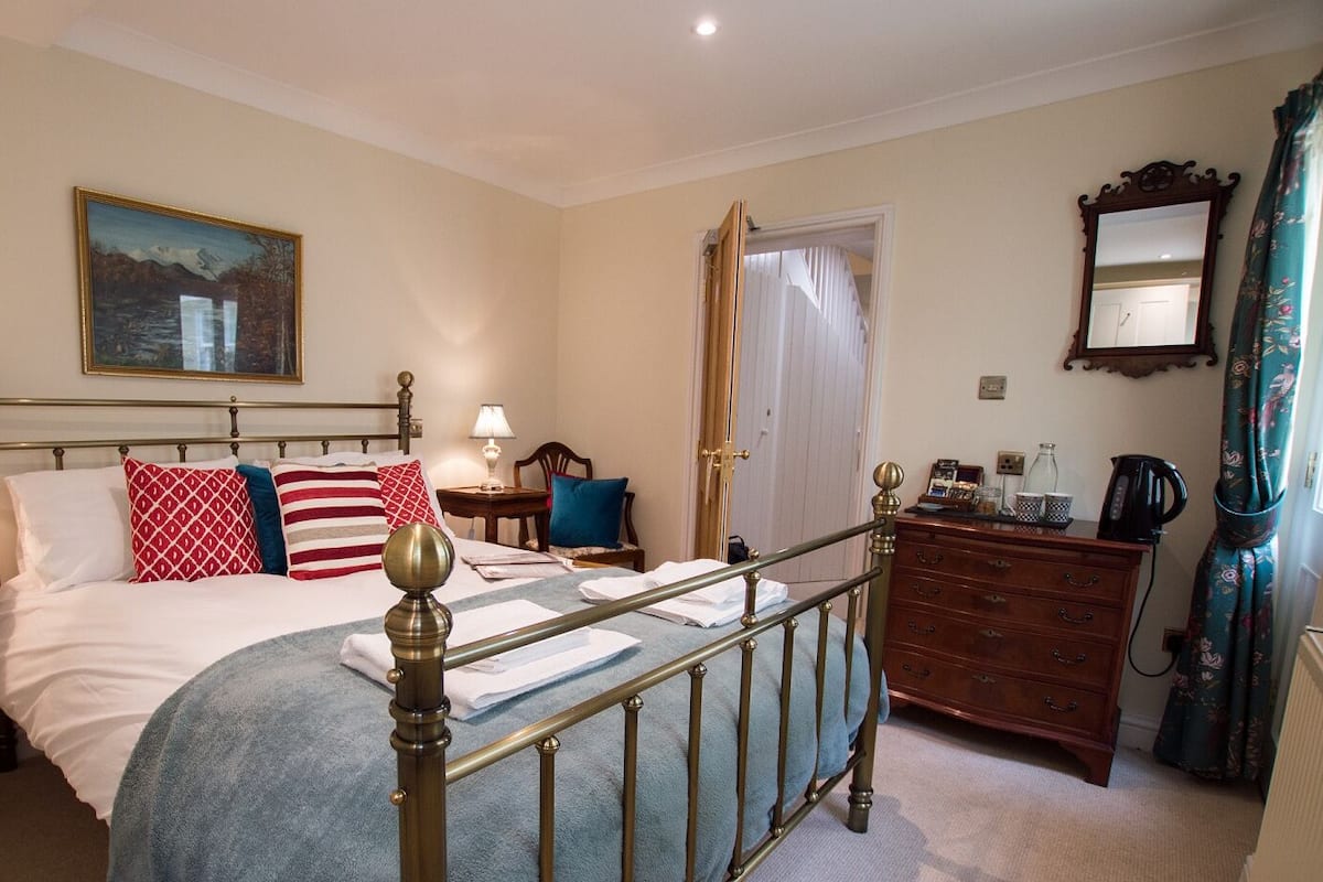 A neatly arranged bedroom with a bed, bedside tables, a dresser, and a mirror.