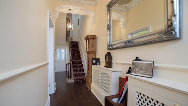 A hallway with a staircase, a mirror, and a radiator. - The Portland Guesthouse (Cheltenham)