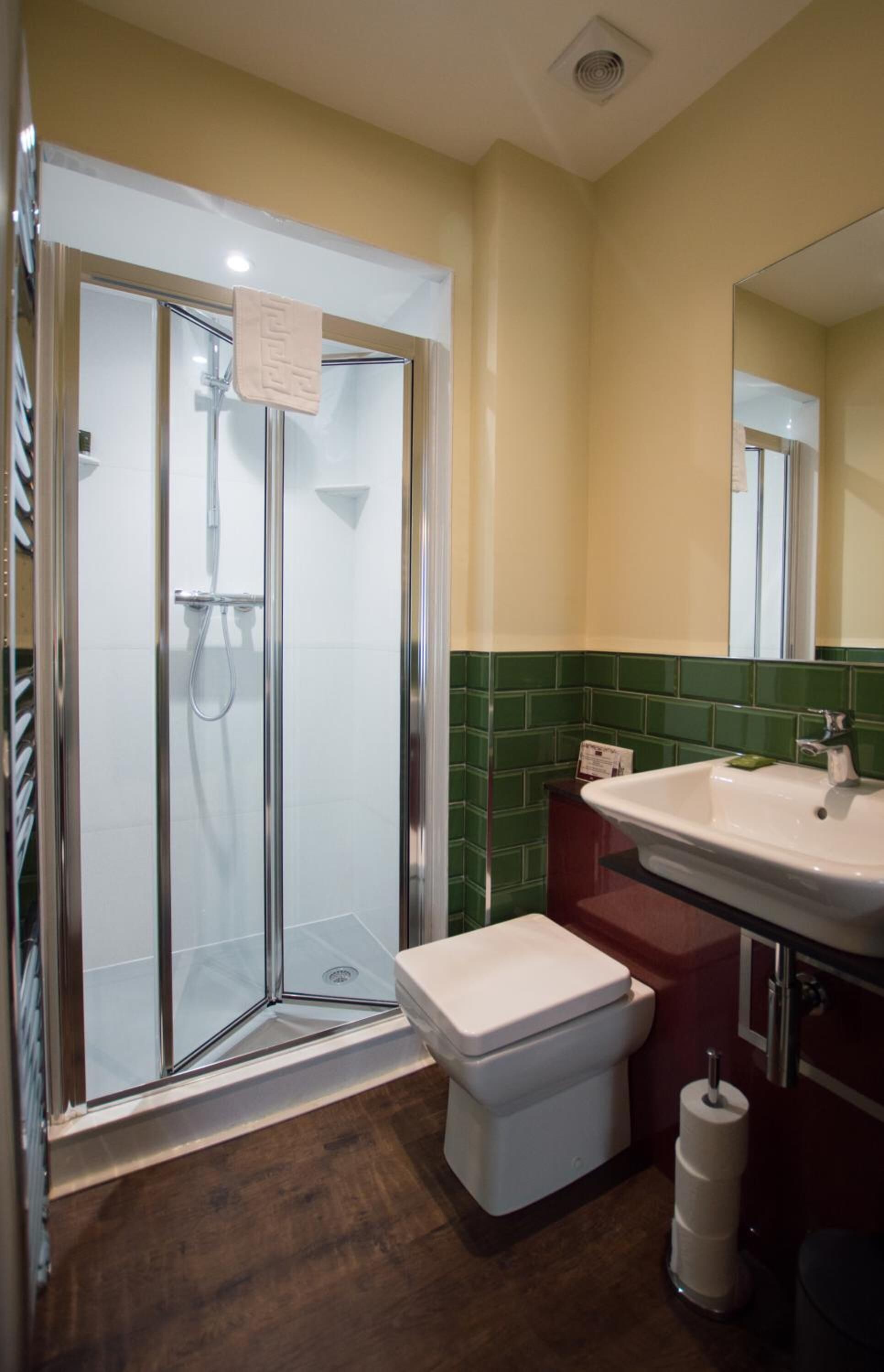 A bathroom with a glass-enclosed shower, a white toilet, a sink with a mirror, and green-tiled walls.