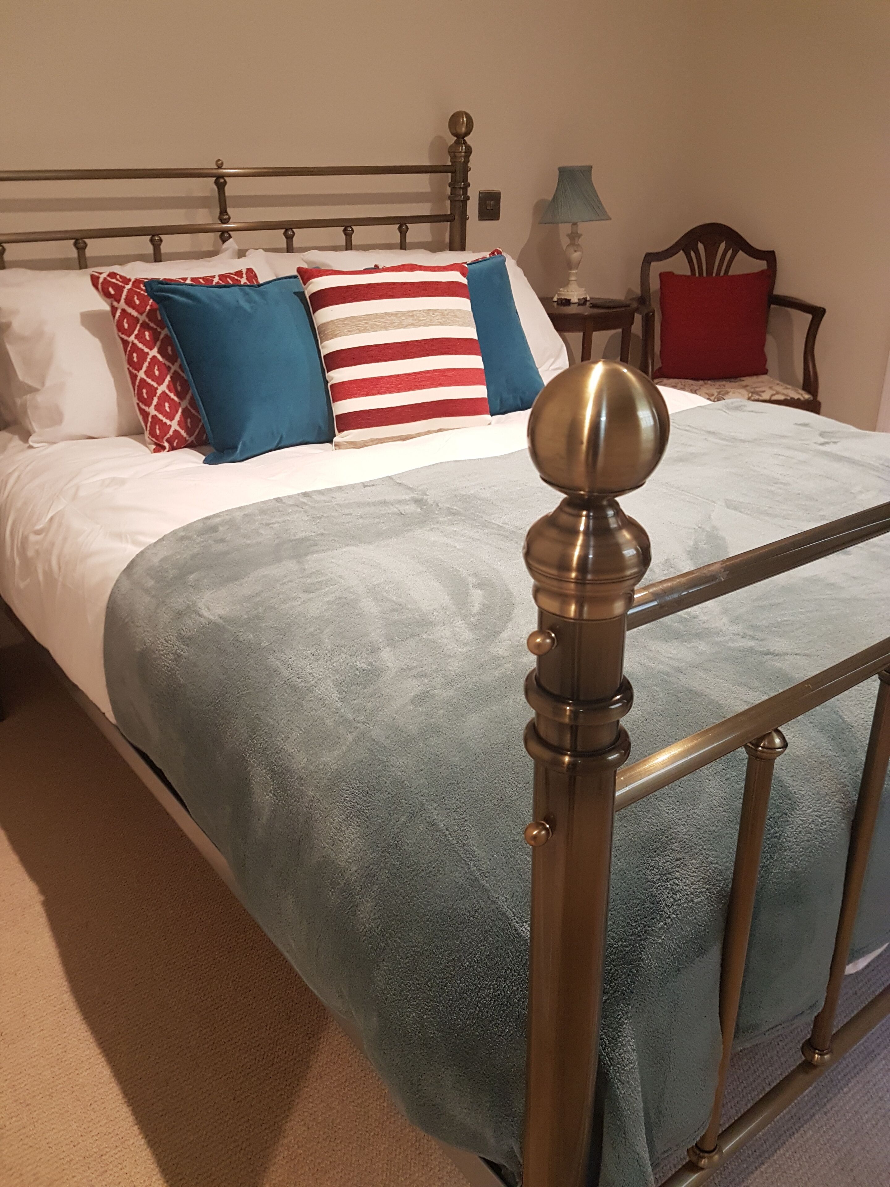 A neatly made bed with a blue blanket and multiple pillows, a wooden headboard, and a bedside table with a lamp.
