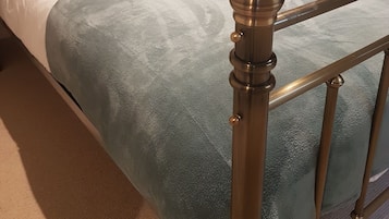 A neatly made bed with a blue blanket and multiple pillows, a wooden headboard, and a bedside table with a lamp.