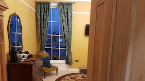 A room with a large window, a dresser, a chair, and a patterned rug. - The Portland Guesthouse (Cheltenham)