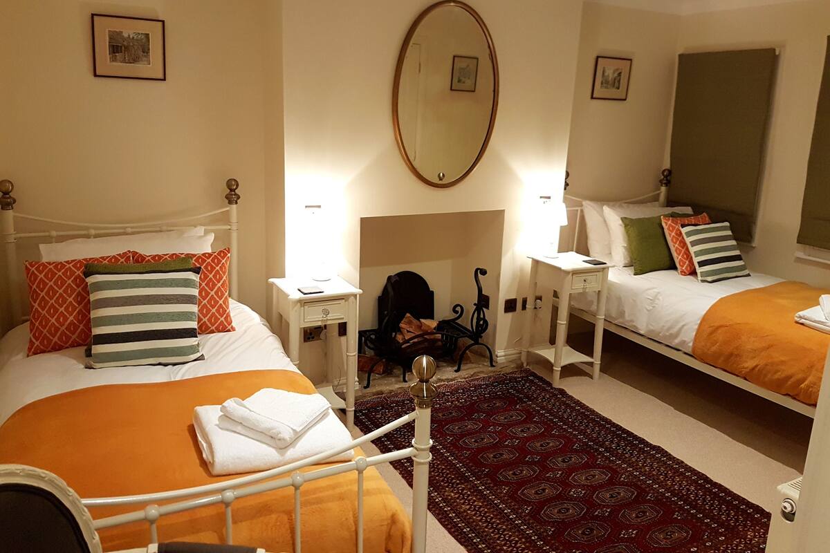 A hotel room with two beds, a large mirror, bedside tables, and a patterned rug.