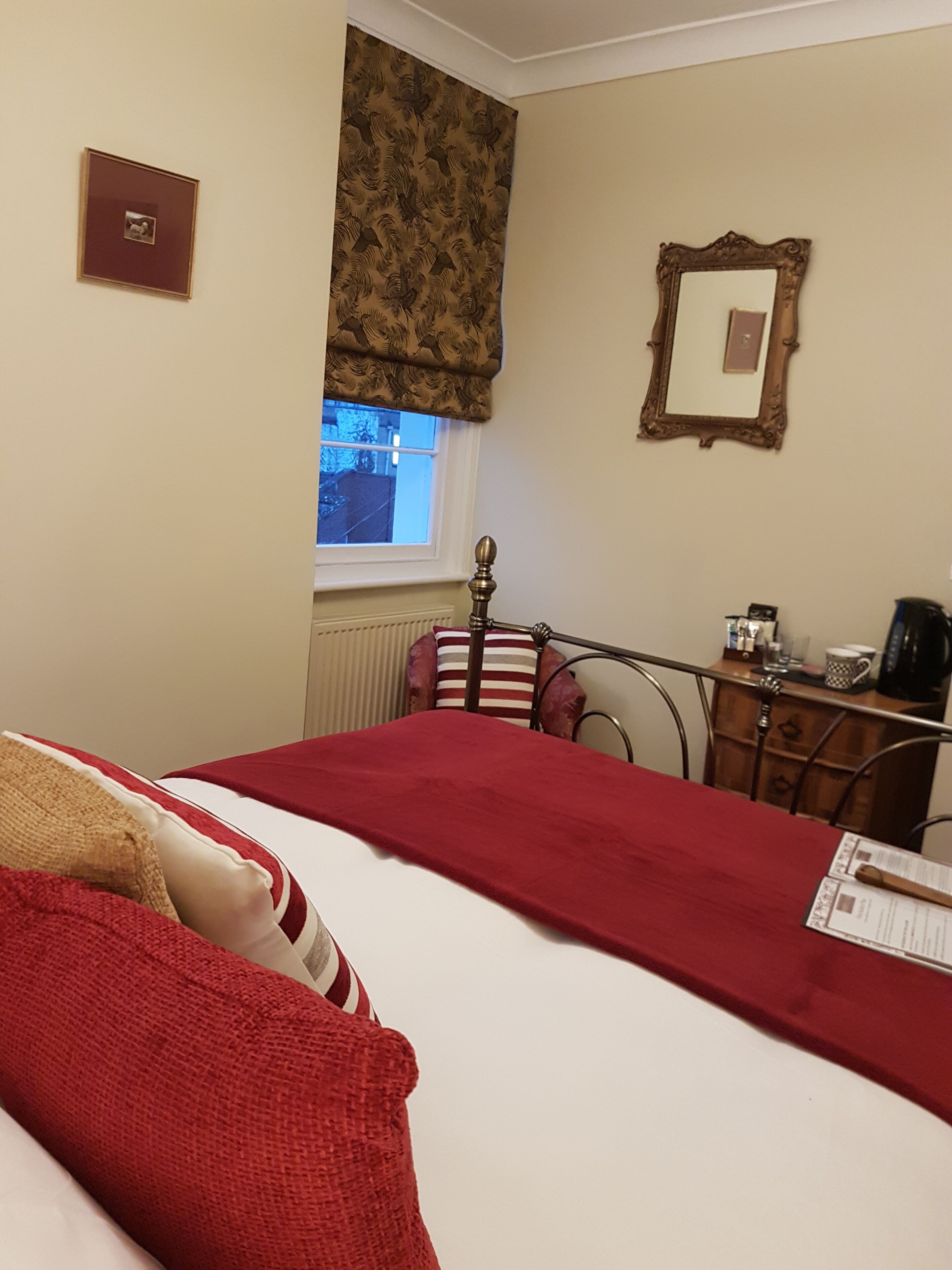 Une chambre d’hôtel avec un lit, une commode, un miroir et une fenêtre avec des rideaux.