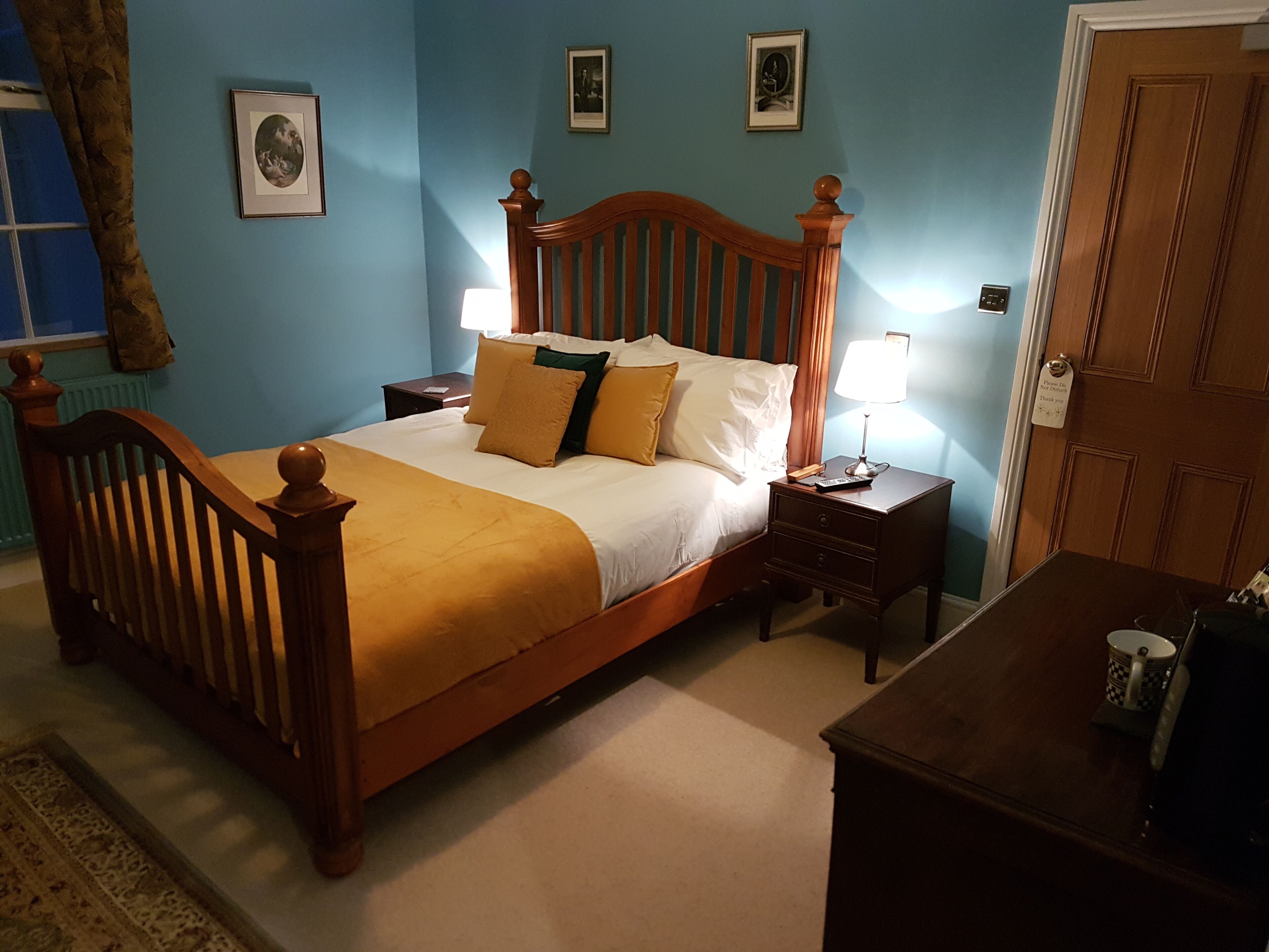A neatly made bed with a wooden headboard, two bedside tables with lamps, a wooden nightstand, and a small table with a cup and a book.
