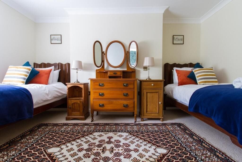 Une chambre double avec deux lits, une commode en bois avec un miroir et un tapis à motifs.