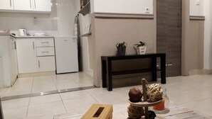 A modern kitchen with white cabinets, a black countertop, and a small refrigerator. There is a wooden box on the floor and a decorative tray with fruits and a candle. - Central Cozy Cute Downtown Studio 1BR (Athens)