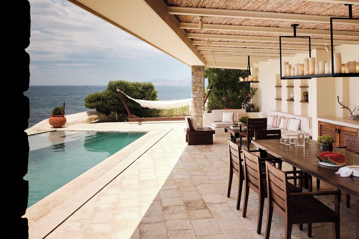 A poolside area with a dining table and chairs, a hanging chair, and a view of the sea.