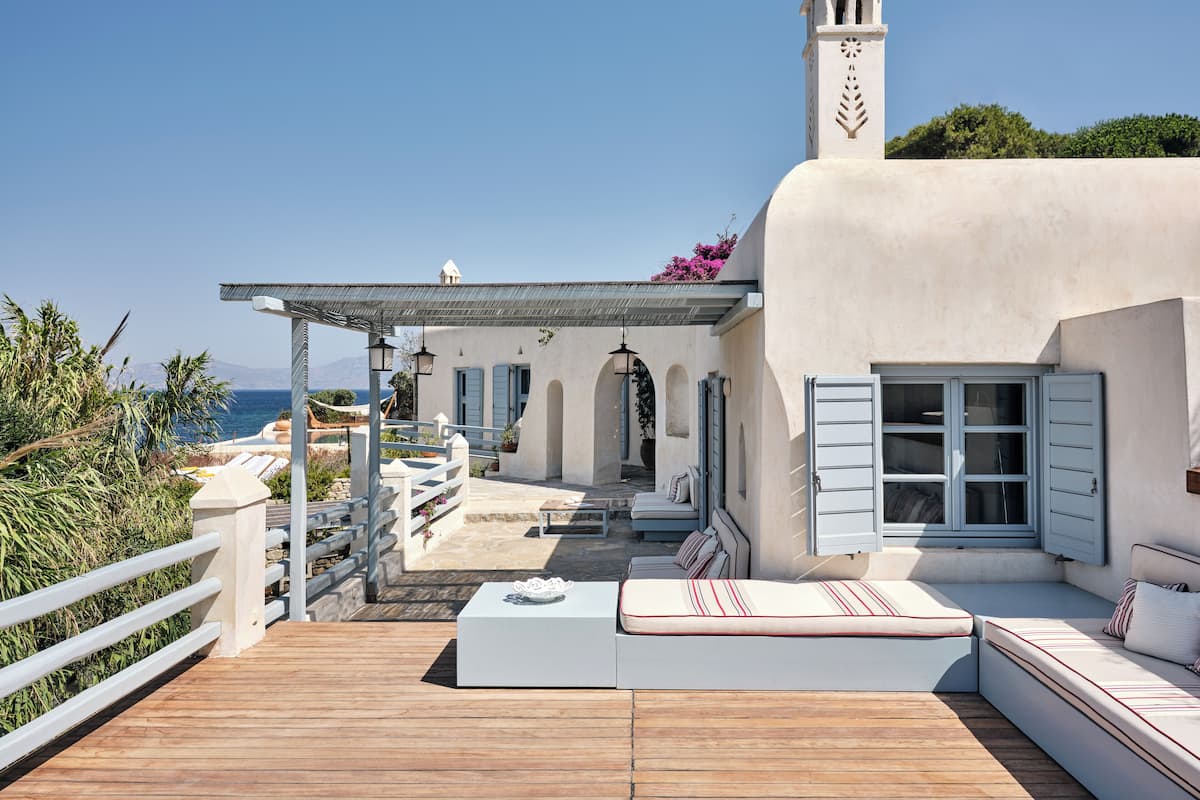 A coastal villa with a wooden deck, outdoor seating, and a view of the sea.