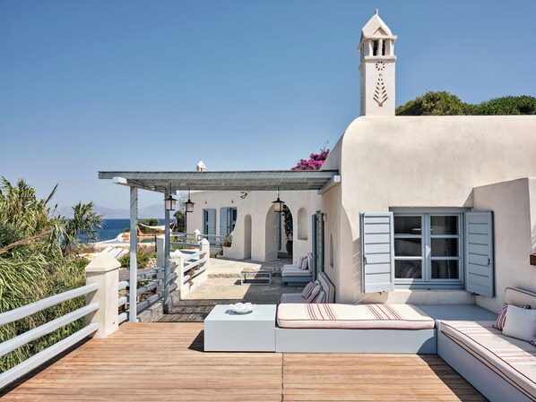 Een landhuis aan de kust met een houten terras, zitplaatsen buiten en uitzicht op zee.