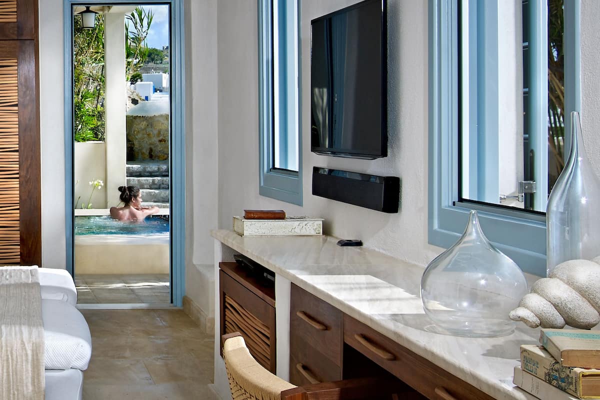 A modern hotel room with a bathtub, a TV, and a view of a pool.