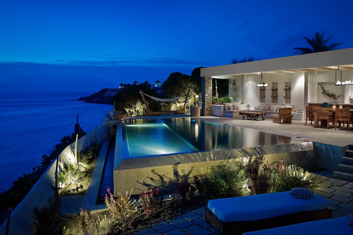 A modern outdoor pool area with a dining setup and a view of the sea.