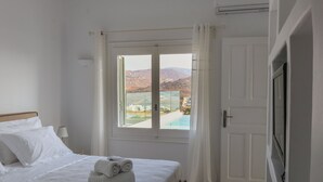 Una habitación de hotel con una cama, un ventanal con vistas a una piscina y montañas, y una puerta.