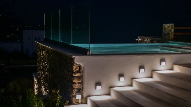 Una terraza en la azotea con vistas al mar, muros de piedra y una serie de escalones que bajan.