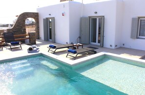 Una piscina con sillones de descanso y un arco de piedra.