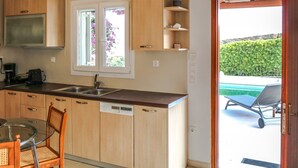 Una cocina con armarios de madera, lavavajillas, pileta doble y ventana con vista a un jardín.