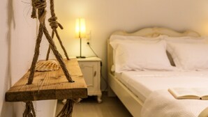 Un dormitorio con una mesita de noche de madera, una lámpara, una cama con ropa blanca y un columpio de cuerda.