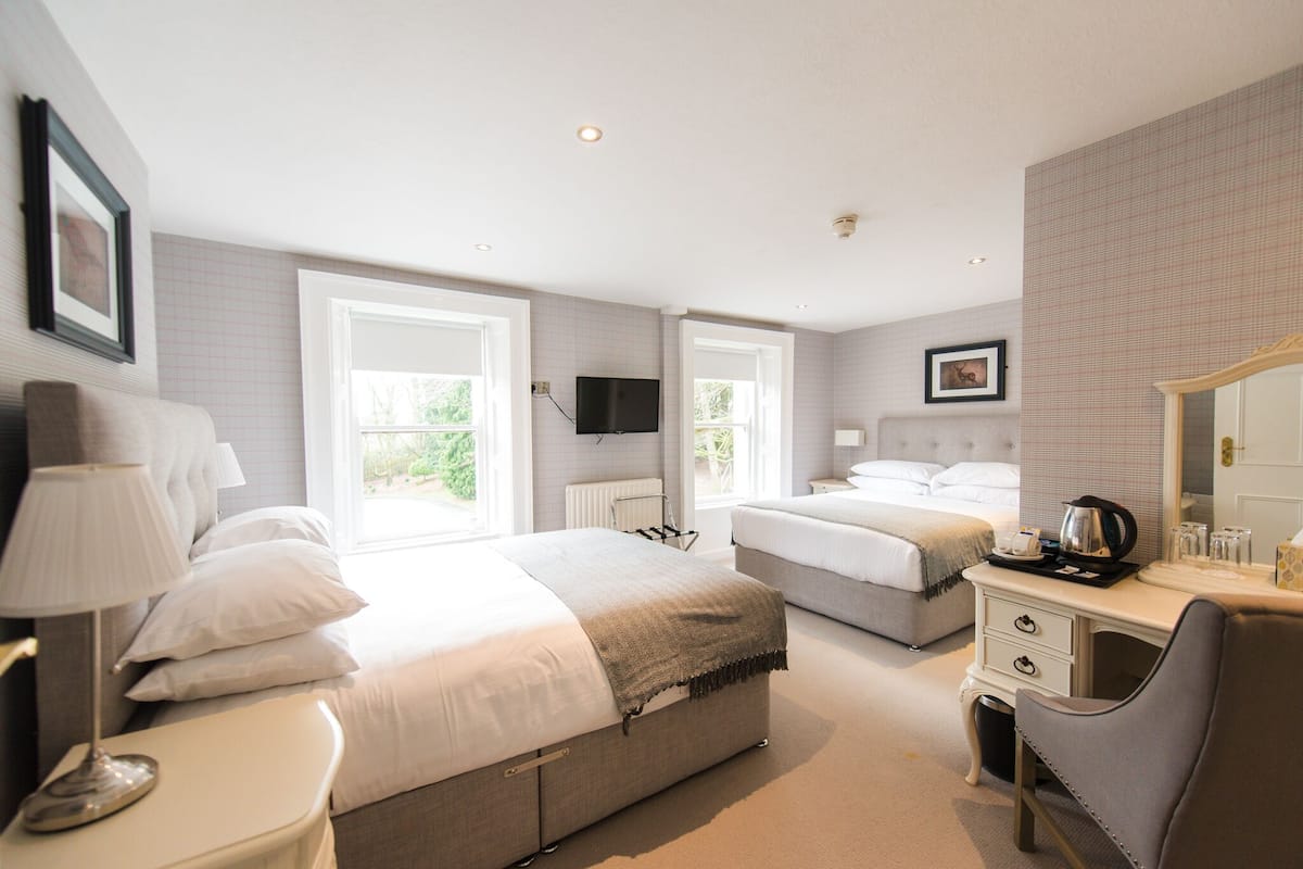 A hotel room with two beds, a desk, a chair, a TV, and a window.