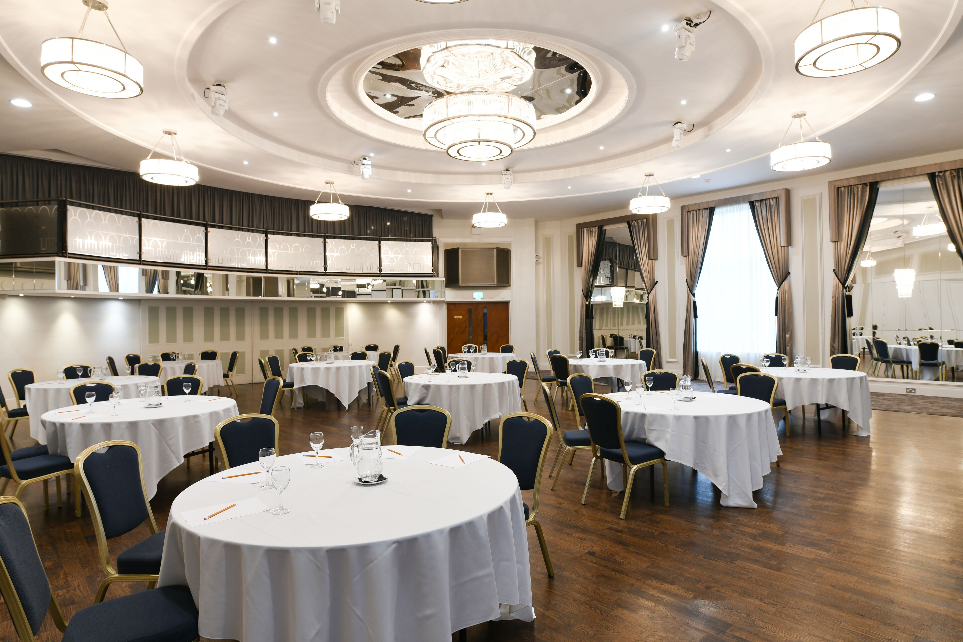 Un salón de conferencias de hotel con varias mesas redondas, sillas y una moderna lámpara de araña.