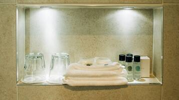 A bathroom vanity with a glass shelf containing toiletries, a towel, and a glass container.