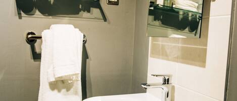 A modern bathroom with a white sink, a glass shelf with toiletries, and a towel rack.
